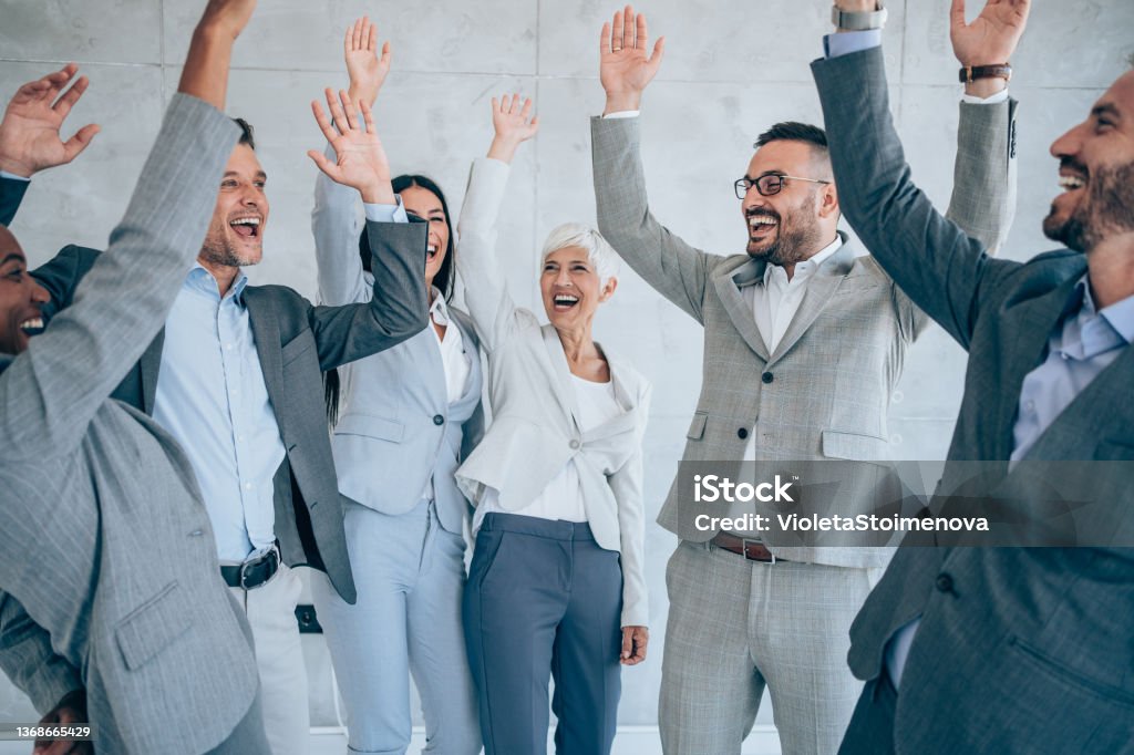 Motivating the team. Shot of group of business people celebrating their success in the office. Multiracial group of corporate business persons on a business meeting in modern office. Cheerful business team raising their hands together in the air. Motivation Stock Photo