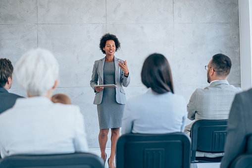 Shot of a businesswoman delivering a speech during a conference. Happy business leader talking to group of her colleagues on a seminar in meeting room.