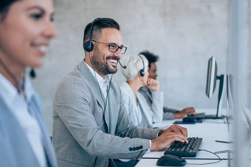 Shot of call center operators working in the office. Call center agent working with his colleagues in modern office. Smiling handsome businessman working in call center.