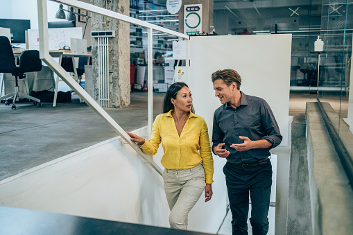 Shot of two colleagues discussing while walking up the stairs in a modern office. Two business people in a motion on stairs in the office.