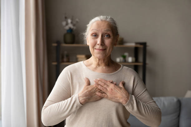 mujer sonriente de mediana edad con las manos cruzadas en el pecho. - senior women caucasian one person religion fotografías e imágenes de stock