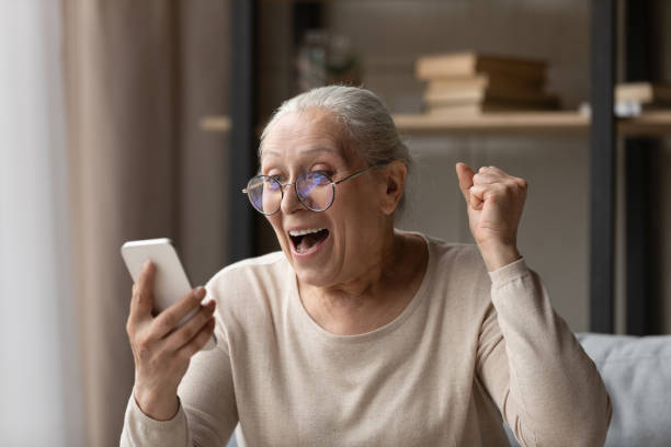 vecchia nonna euforica che ride celebrando la vincita alla lotteria online. - shock grandmother surprise senior adult foto e immagini stock