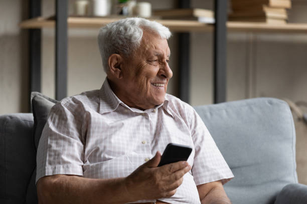 istock Dreamy smiling old man using cellphone at home. 1368666503