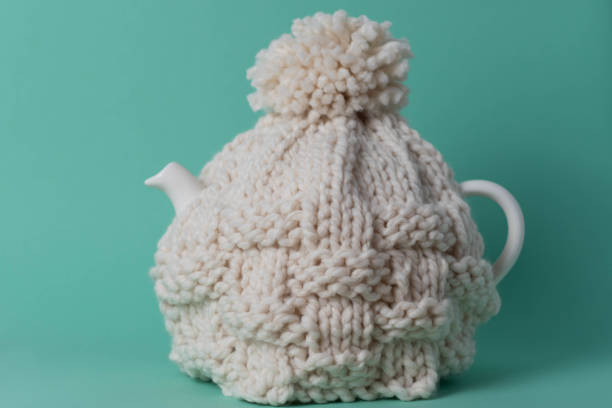 Teapot with a knitted tea cosy on green background stock photo