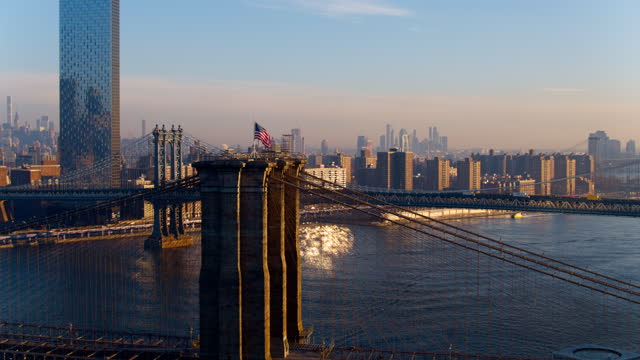 Remote view of Midtown Manhattan across East River, over the Brooklyn Bridge and Manhattan Bridge. Drone video with the cinematic wide panning-orbiting camera motion.