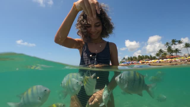 Young woman feeding fish on tropical beach