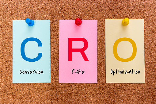 Conceptual 3 letters keyword CRO (Conversion Rate Optimization) on multicolored stickers attached to a cork board.
