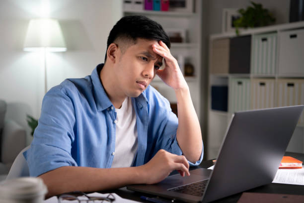 unglücklicher junger asiatischer mann, der ernsthaft und besorgt auf den laptop-bildschirm schaut - frustration computer confusion businessman stock-fotos und bilder