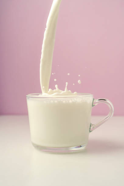 istock Milk is poured into a transparent cup on a purple background. 1368706593