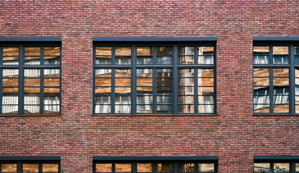 Facade wall of a brick building with windows. The opposite wall reflected in the window pane. Smooth rows of old masonry.