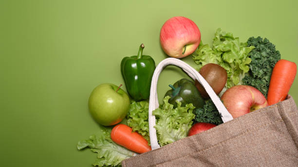 istock Eco bag with assorted raw organic vegetables and fruits on green background. 1368708582
