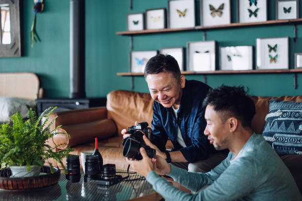 istock Smiling senior Asian father and son with their camera and camera lens collection, sharing their common interest and hobbies together at home 1368710394