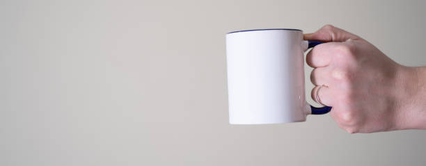 istock White mug in the hands of a man on a light background. 1368714005