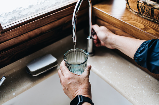 Personal perspective of man filling a glass of filtered water right from the tap in the kitchen at home