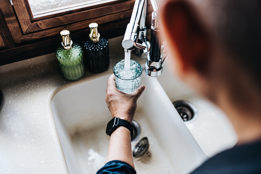 Vista sobre el hombro de un hombre asiático mayor llenando un vaso de agua filtrada directamente desde el grifo de la cocina de la casa photo