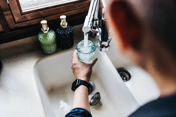 Photo of Over the shoulder view of senior Asian man filling a glass of filtered water right from the tap in the kitchen at home