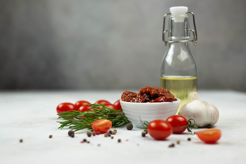 Sun dried tomatoes with fresh herbs, spices, tomatoes, olive oil and garlik. Grey background.