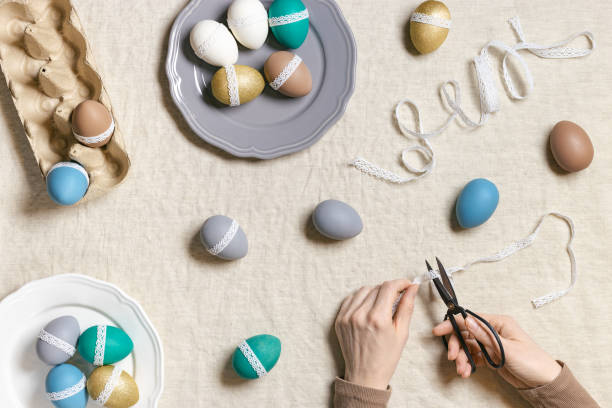 istock Decoration Easter eggs, female hands decorating colorful chicken egg with white tape lace, traditional celebration food and holiday symbol.  Home preparing for Happy Easter. Top view 1368732815
