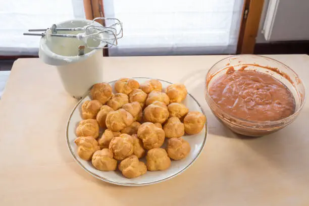 Ingredients for the preparation of profiteroles filled with whipped cream and covered with chocolate. Plate of empty puffs to fill and chocolate cream