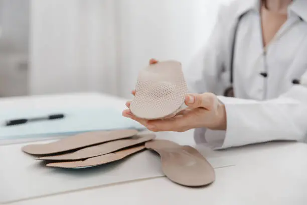 Doctor holding an insole while sitting at a table. Orthopedist tests the medical device. Orthopedic insoles. Foot care. Flat Feet Correction. Treatment and prevention of flat feet and foot diseases.