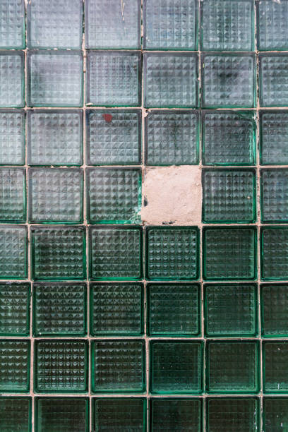 Old square glass blocks wall. One block broken and sealed with cement.