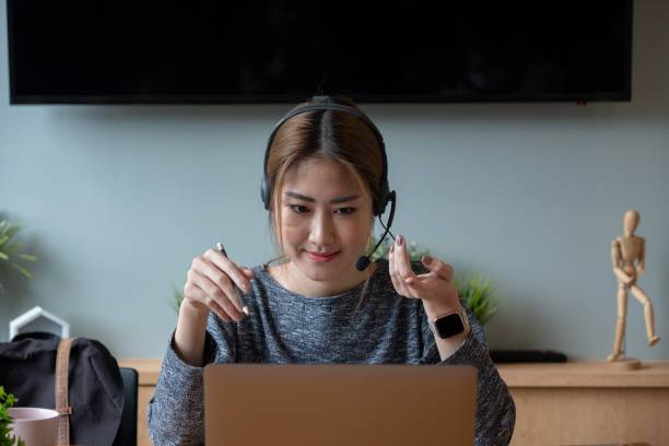 istock Shot smiling asian woman freelancer wearing headset, communicating with client via video computer call. Millennial pleasant professional female tutor giving online language class 1368744008