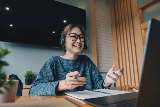 Photo of Asian woman wear headphones look at laptop enjoy study online with tutor, listen audio lecture watch webinar prepare for exams, e-learn, self education concept