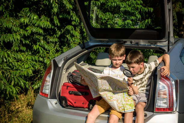 istock Two cute boys sitting in a car trunk before going on vacations with their parents. Kids sitting in a car examining a map. Summer break at school. Family travel by car 1368745863