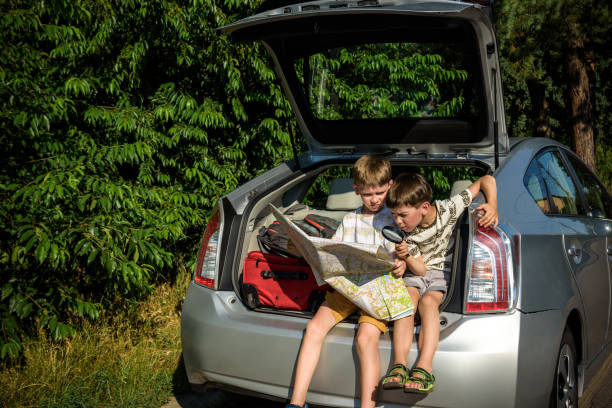 istock Two cute boys sitting in a car trunk before going on vacations with their parents. Kids sitting in a car examining a map. Summer break at school. Family travel by car 1368745867