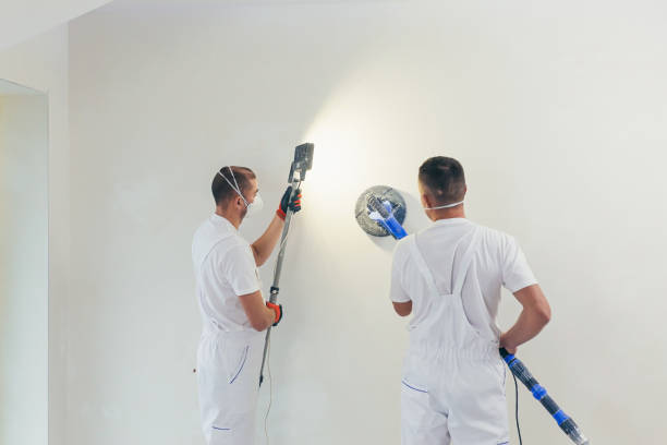 istock Plasterer smoothes the wall surface with a wall grinder. Two master builders grind a white plaster wall. a man in overalls grinds the surface in a respirator. experienced repairman 1368751643