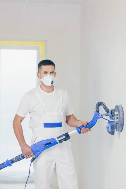 istock Plasterer smoothes the wall surface with a wall grinder. Two master builders grind a white plaster wall. a man in overalls grinds the surface in a respirator. experienced repairman 1368751645