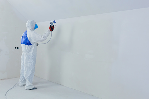 Airless spray paint. The worker paints the wall with an airless spray in white, an experienced worker sprays the paint on the surface with a mechanical air tool