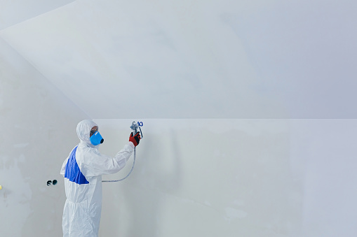 Airless spray paint. The worker paints the wall with an airless spray in white, an experienced worker sprays the paint on the surface with a mechanical air tool