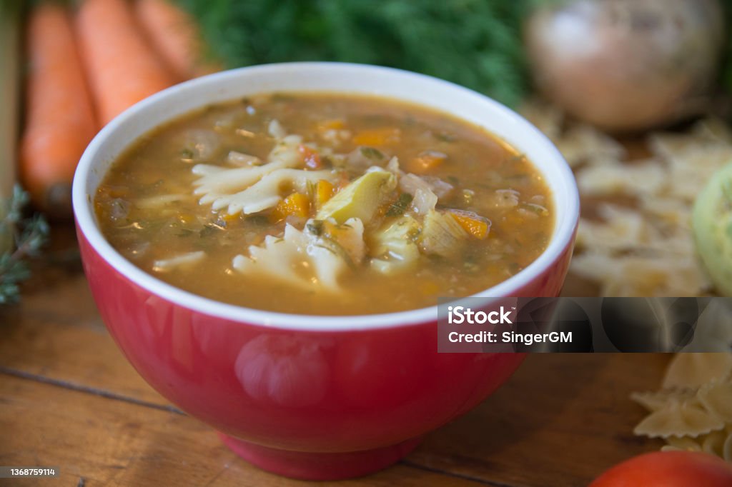 Minestrone soup, a typical thick vegetables soup, originally from Italy, served in a red bowl with Farfalle Pasta. Minestrone Stock Photo