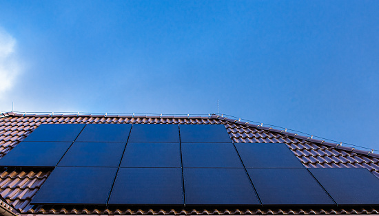 Modern full black solar panels on the brown ceramic tiles roof of a house.