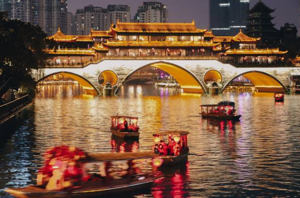 Stream of little tour boats on the Jinjiang River at night, passing the Anshun Bridge, in Chengdu, Sichuan, China Stream of little tour boats with red lanterns on the Jinjiang River at night, passing the iconic, traditional and illuminating Anshun Bridge in Chengdu, Sichuan, China. Chengdu a vibrant mega city in China. chengdu photos stock pictures, royalty-free photos & images