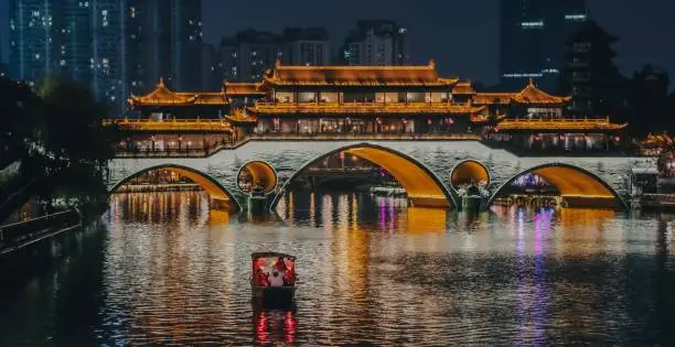 Beautiful landscape of Chengdu at night, a tour boat floats by the famous Anshun Bridge on the Jinjiang River, Chengdu, Sichuan, China. Chengdu a vibrant mega city in southwest China.