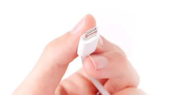 Photo of Hand holding a simple white USB type C mobile phone smartphone charger cable, digital data transfer, charging, power concept, phone accessories. USB C cable plug end detail, macro, extreme closeup