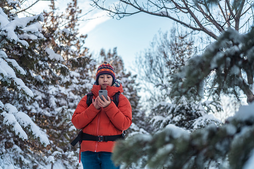 A young female backpacker traveler is using her smart phone in forest in winter.