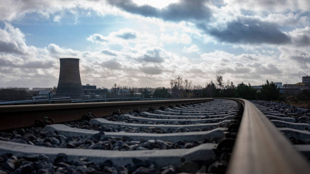 Detail of railroad tracks in the foreground and a cooling tower of a power plant in the background. Cloudy sky. Renewable energy concept.