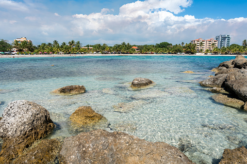 Crystal clear aqua blue water and white sandy beach with large lava rocks in foreground.