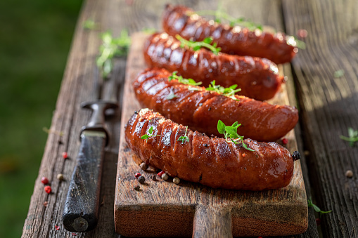 Spicy roasted sausages on wooden plate in garden. Grilled sausages with herbs and spicy spices.