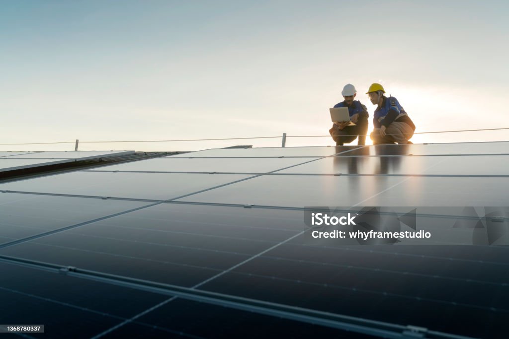 Specialist technician professional engineer with laptop and tablet maintenance checking installing solar roof panel on the factory rooftop under sunlight. Engineers team survey check solar panel roof. Solar Panel Stock Photo