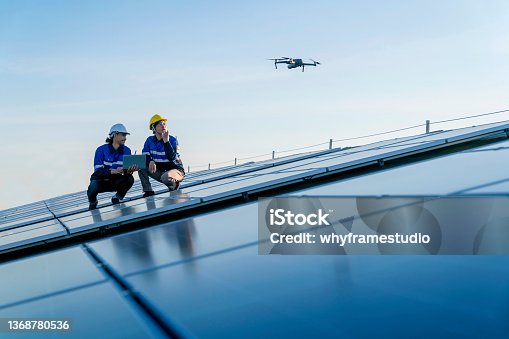istock Specialist technician professional engineercontrol drone checking top view of installing solar roof panel on the factory rooftop under sunlight. Engineers holding tablet check solar roof. 1368780536