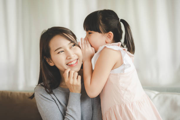 Asian daughter girl whispering I love you to mother Little Asian daughter girl whispering I love you mommy to happy smiling mother in living room asian daughter stock pictures, royalty-free photos & images