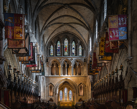 Dublin, Ireland, August 2019 Flags and pennants on both sides of illuminated altar in St. Patricks Cathedral with arches and stained glass