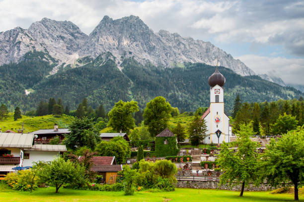 villaggio bavarese grainau. chiesa a cupola st. johannes, cimitero e case con montagne, cime waxenstein e zugspitze. - grainau foto e immagini stock