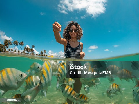istock Young woman feeding fish on tropical beach 1368808461