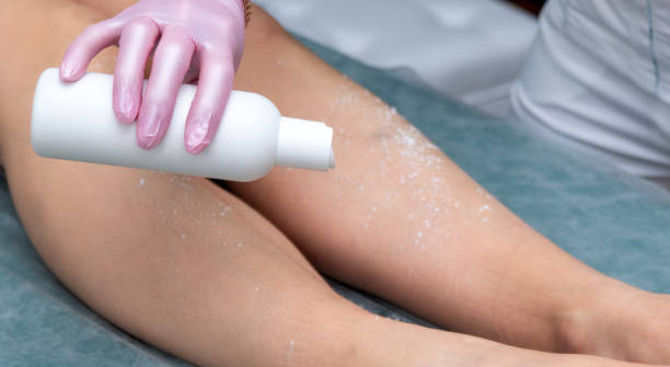The hand holds the bottle and pours talcum powder on the client's feet before depilation. Selective focus. stock photo