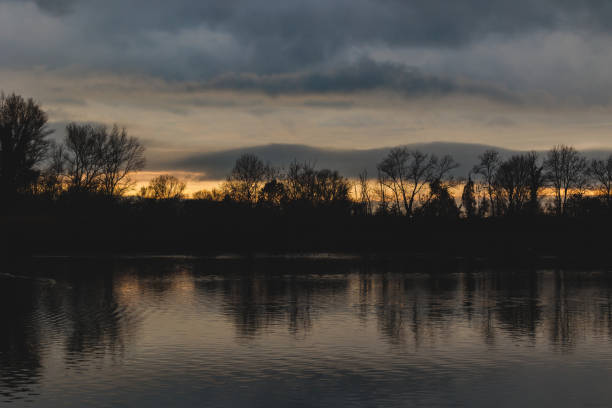wide angle view of a wetland environment and a wood with calm water and a variable cloudy sky at sundown